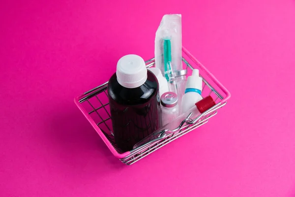 Medicines in a shopping cart for a supermarket shopper on a pink paper background. The concept of medicine and the cost of treatment