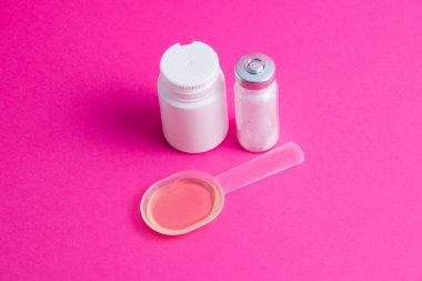 İlaçlı ampul, tıbbi karışım ve pembe arka planda beyaz bir kavanoz hap..