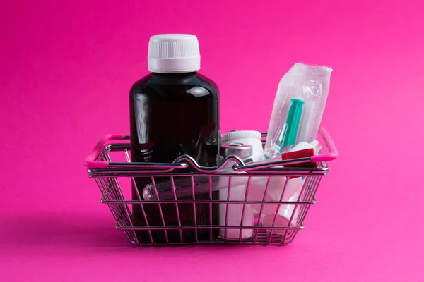 Medicines in a shopping cart for a supermarket shopper on a pink paper background. The concept of medicine and the cost of treatment