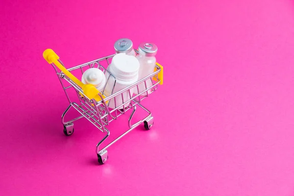 Medicines, drops in a metal trolley for a buyer from a supermarket on a pink paper background. The concept of medicine and the cost of treatment