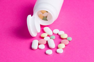 Pembe kağıt arkaplanda çok renkli haplar ve beyaz kavanoz. Üst görünüm kopyala.