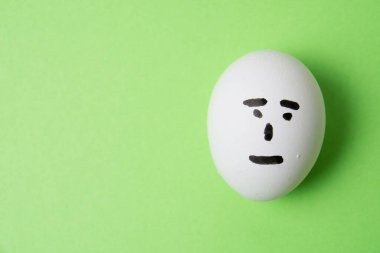 Yüzünde kayıtsız bir duygu olan bir yumurta, yeşil arka plan fotokopi alanı