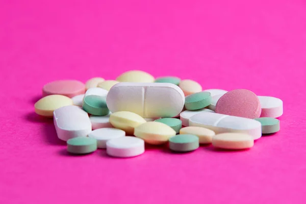 Many multicolored vitamins and pills on a pink background copy space, close-up.