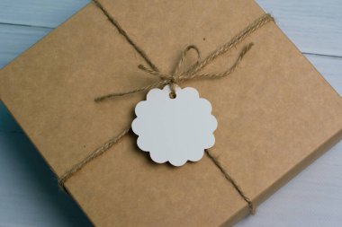 Kırsal tarzda bir halatla bağlanmış bir hediye kutusu, beyaz etiketli, açık ahşap arka planda, metin eklemek ve kopyalamak için yer