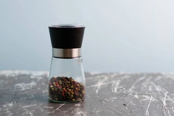 Glass pepper mill with a mixture of peppercorns, on a light background, horizontal format and copy space
