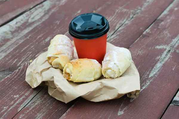 Coffee and sweet buns with jam on a wooden table. Paper cup and food to go. The concept of outdoor recreation