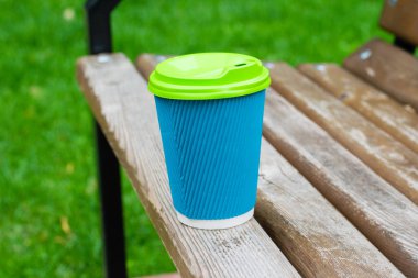 Bulutlu bir günde, bir yaz parkında, ahşap bir bankta kahve bardağı, kopyalama alanı. Park eğlencesi konsepti.