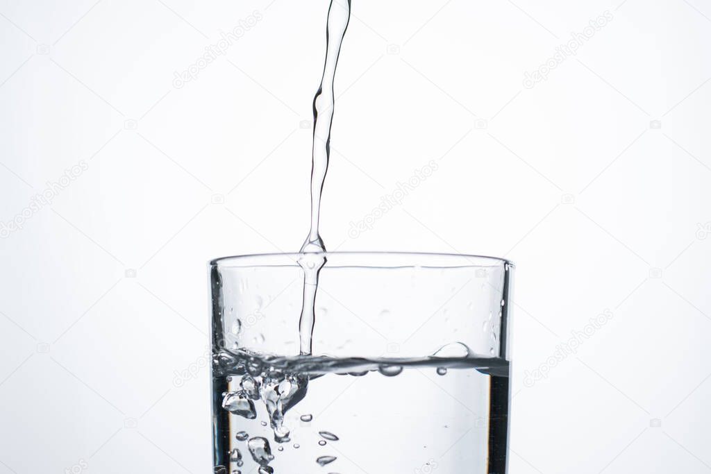 Jet of water or alcohol is pouring into a glass with splashes and bubbles, copy space.