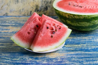 Beyaz bir tabakta olgun karpuz dilimleri ve arka planda yarım karpuz. Yaz tatili konsepti ve uygun beslenme