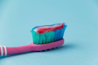 Eski pembe bir diş fırçasında çok renkli bir diş macunu. Arka planda mavi bir kağıt var. Diş ve sakız bakımı kavramı.