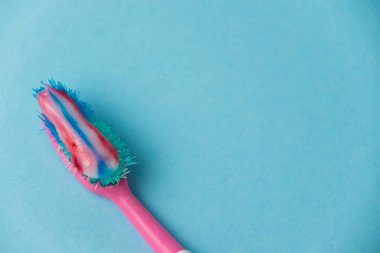 Eski pembe bir diş fırçasında çok renkli bir diş macunu. Arka planda mavi bir kağıt var. Diş ve sakız bakımı kavramı.
