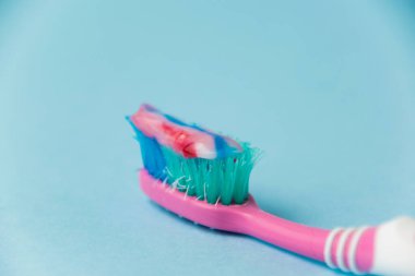 Eski pembe bir diş fırçasında çok renkli bir diş macunu. Arka planda mavi bir kağıt var. Diş ve sakız bakımı kavramı.