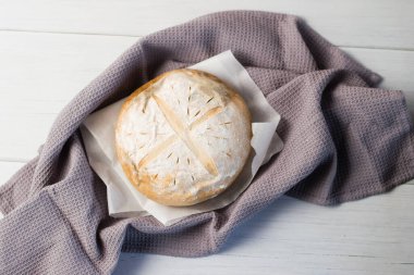 Gri bir havlunun üzerindeki ışık masasında taze pişmiş lezzetli beyaz ekmek. Lezzetli ev yapımı yemekler..