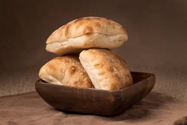 Tahta bir kaseye yerleştirilmiş üç ciabatta rulosunun stüdyo fotoğrafı..