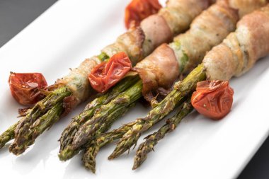 Pastırmaya sarılı aspargus mızrakları beyaz bir tabakta sergilenir..