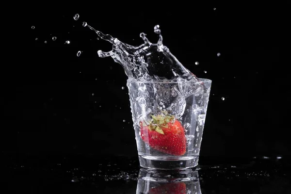 草莓和冰块在黑色背景下掉进水杯的摄影棚照片 — 图库照片