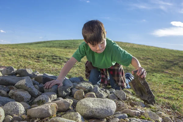Rapaz olha debaixo de uma rocha . — Fotografia de Stock