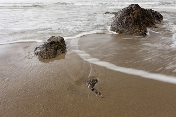 在海滩上的岩石周围水奔涌. — 图库照片
