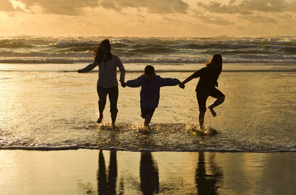 Família corre no surf ao pôr-do-sol . — Fotografia de Stock