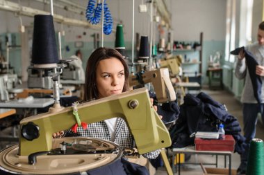 Bir iş parçasını analiz eden genç bir adamın ve tekstil endüstrisinde örgü ören makineyle çalışan bir kadının fotoğrafını çek.
