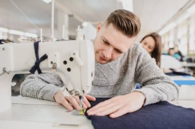 Bir fabrikada dikiş makinesiyle dikiş diken genç bir adam ve diğer terzilerin fotoğrafını çek.