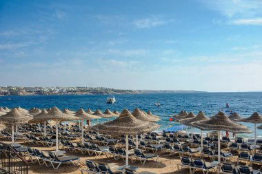 Yaz tatili için cennet gibi bir tropik tatil beldesindeki kumsalda Thatched plaj şemsiyeleri ve şezlongları