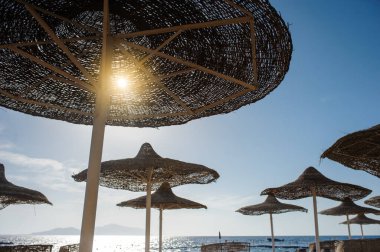 Yaz tatili için cennet gibi bir tropik tatil beldesindeki kumsalda Thatched plaj şemsiyeleri ve şezlongları