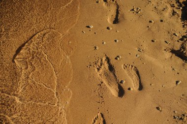 Sahildeki suyun yakınındaki kumda insan ayağının izleri var.