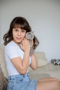 Kollarında gri bir kedi yavrusu olan seksi bir esmerin yakın plan fotoğrafı.