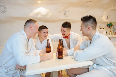 Beyaz önlüklü dört adamın bir masanın etrafında oturup sauna işleminden sonra bira içerken fotoğrafını çek.