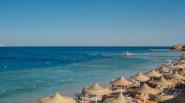 Yaz tatili için cennet gibi bir tropik tatil beldesindeki kumsalda Thatched plaj şemsiyeleri ve şezlongları