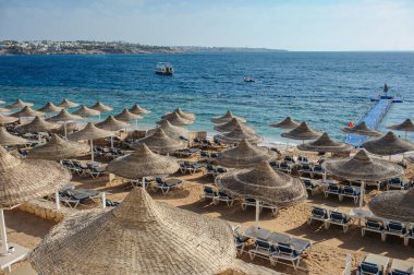 Yaz tatili için cennet gibi bir tropik tatil beldesindeki kumsalda Thatched plaj şemsiyeleri ve şezlongları