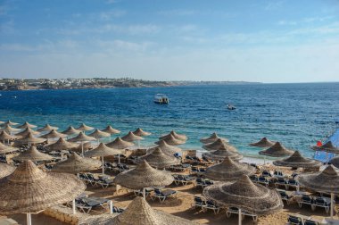 Yaz tatili için cennet gibi bir tropik tatil beldesindeki kumsalda Thatched plaj şemsiyeleri ve şezlongları