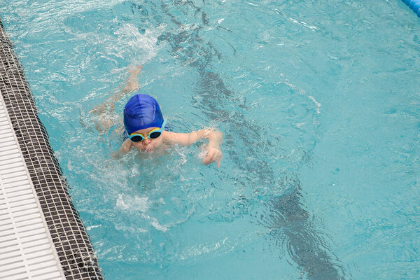 вид сверху на 7-летнего мальчика, играющего и плавающего в бассейне