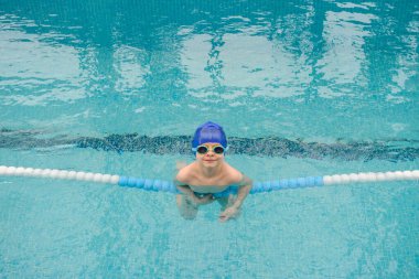 Yüzme havuzunda oynayan ve yüzen 7 yaşındaki bir çocuğun gülümsemesi ve gülmesi.