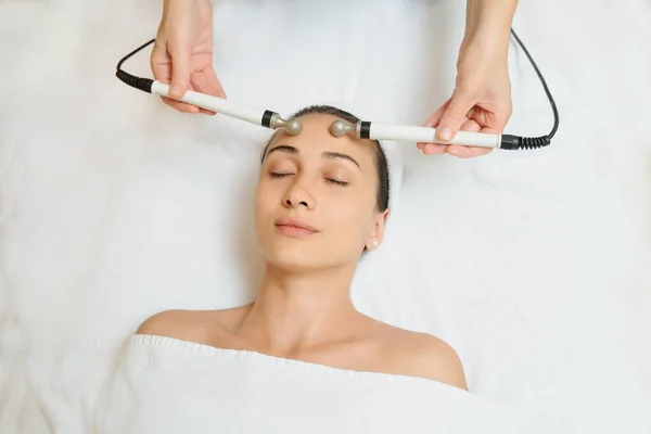 Top view of middle aged woman receiving electrical stimulation facial skin care spa procedure. Micro-current lift face. Beauty spa procedure. Anti aging rejuvenation non surgical treatment in medical center.