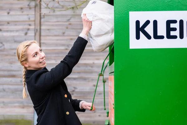 Woman putting old or used clothes into donation bin — Stock Photo, Image