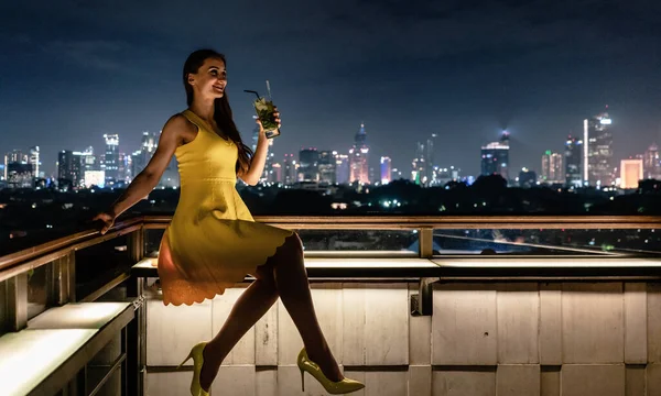 Женщина выпивает на террасе на крыше с видом на город — стоковое фото