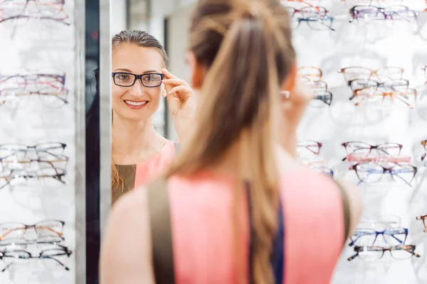 Jonge vrouw probeert modieuze bril in optometrist winkel — Stockfoto