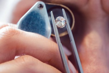Jeweler looking at precious stone through a loupe clipart