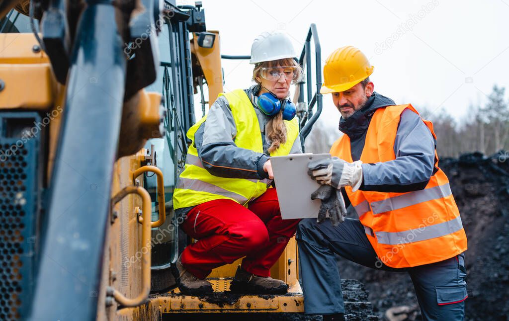 Woman and man worker in quarry on excavation machine
