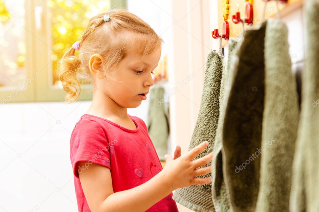 Little girl in nursery school using towel in bathroom