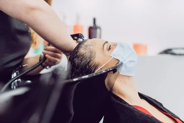 Mujer con mascarilla en una peluquería durante el lavado de har —  Fotos de Stock