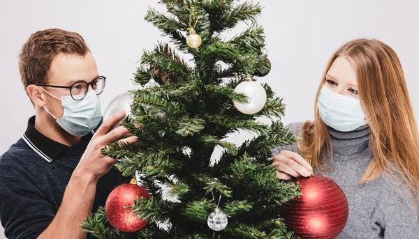 Ζευγάρι στολίζει το χριστουγεννιάτικο δέντρο φορώντας μάσκα προσώπου covid-19 — Φωτογραφία Αρχείου