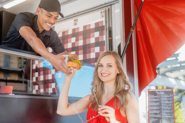 Hermosa mujer conseguir una hamburguesa como comida para llevar de cocinero en camión de comida — Foto de Stock