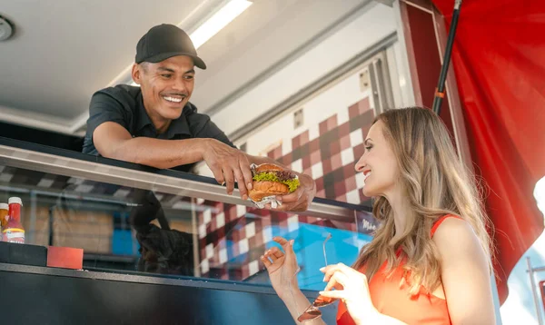 Cocinar en un camión de comida entrega sabrosa hamburguesa a cliente mujer — Foto de Stock