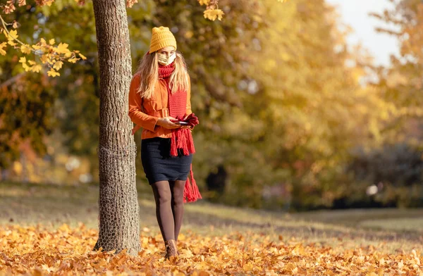 Femme inquiète vérifiant son téléphone portant un masque en automne — Photo