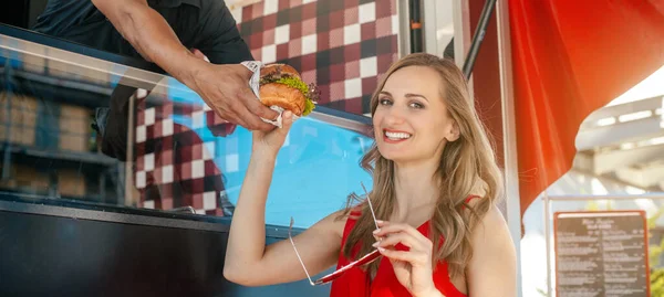 Красива жінка отримує бургер як виймає їжу з кухаря в харчовій вантажівці — стокове фото