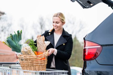 Alışveriş yaptıktan sonra arabasının bagajına alışveriş yapan bir kadın.