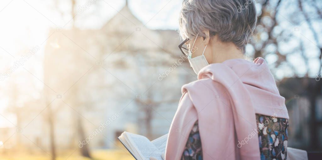 Senior lady with face mask reading the bible in front of a church